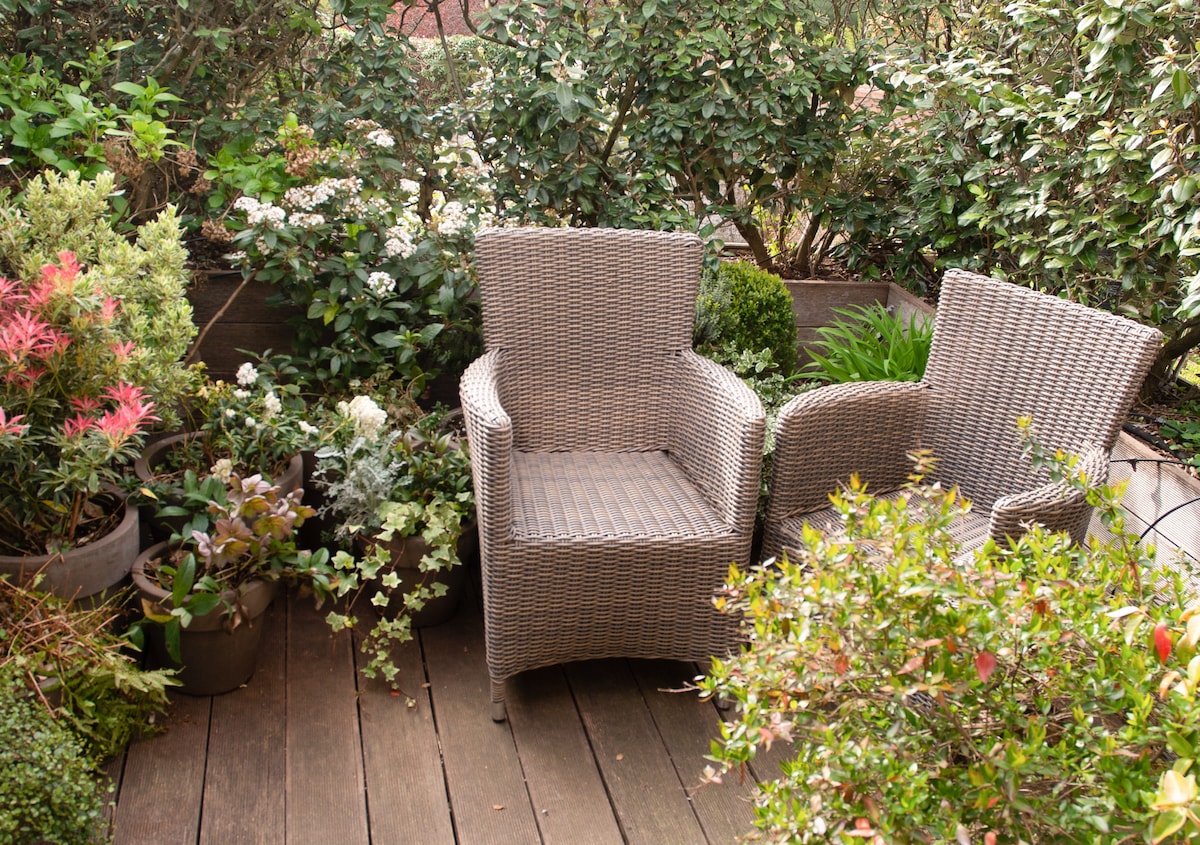 A serene outdoor terrace is equipped with two wicker chairs surrounded by lush greenery. Various potted plants display a range of colors and textures, creating a peaceful setting that invites relaxation.