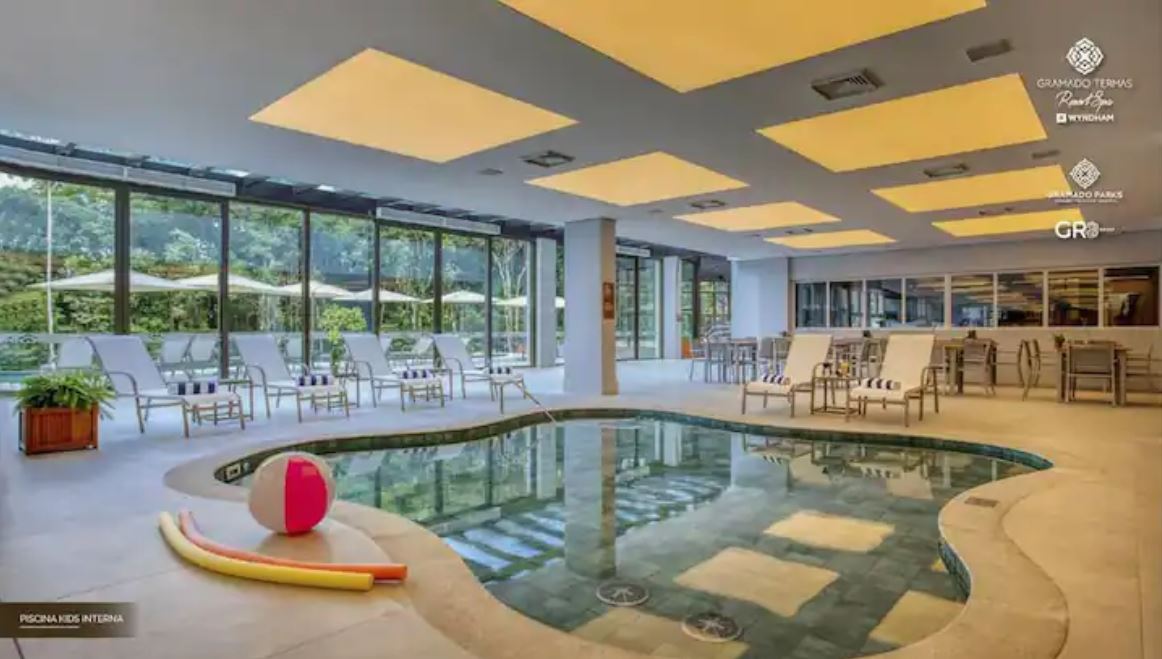 An indoor heated pool is surrounded by lounge chairs, offering a relaxing space for guests. Natural light filters through large windows, illuminating the area. Colorful pool floats add a playful touch to the tranquil environment.