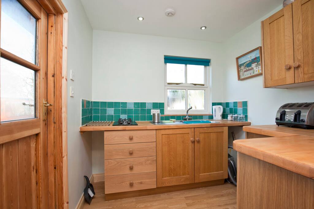 Small kitchen equipped with microwave, 2 burner gas hob, fridge and toaster.