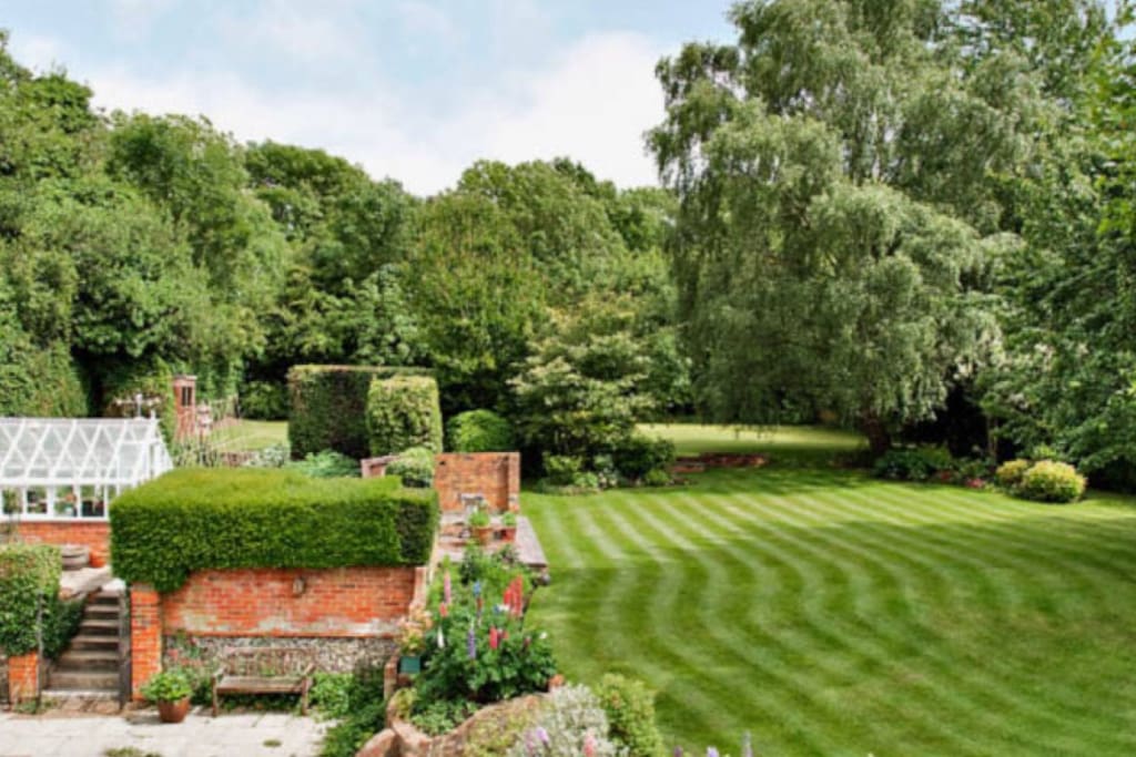 View of garden from house with top lawn football / games pitch visible at the back of the garden. Trampoline & paddling pool behind green house.