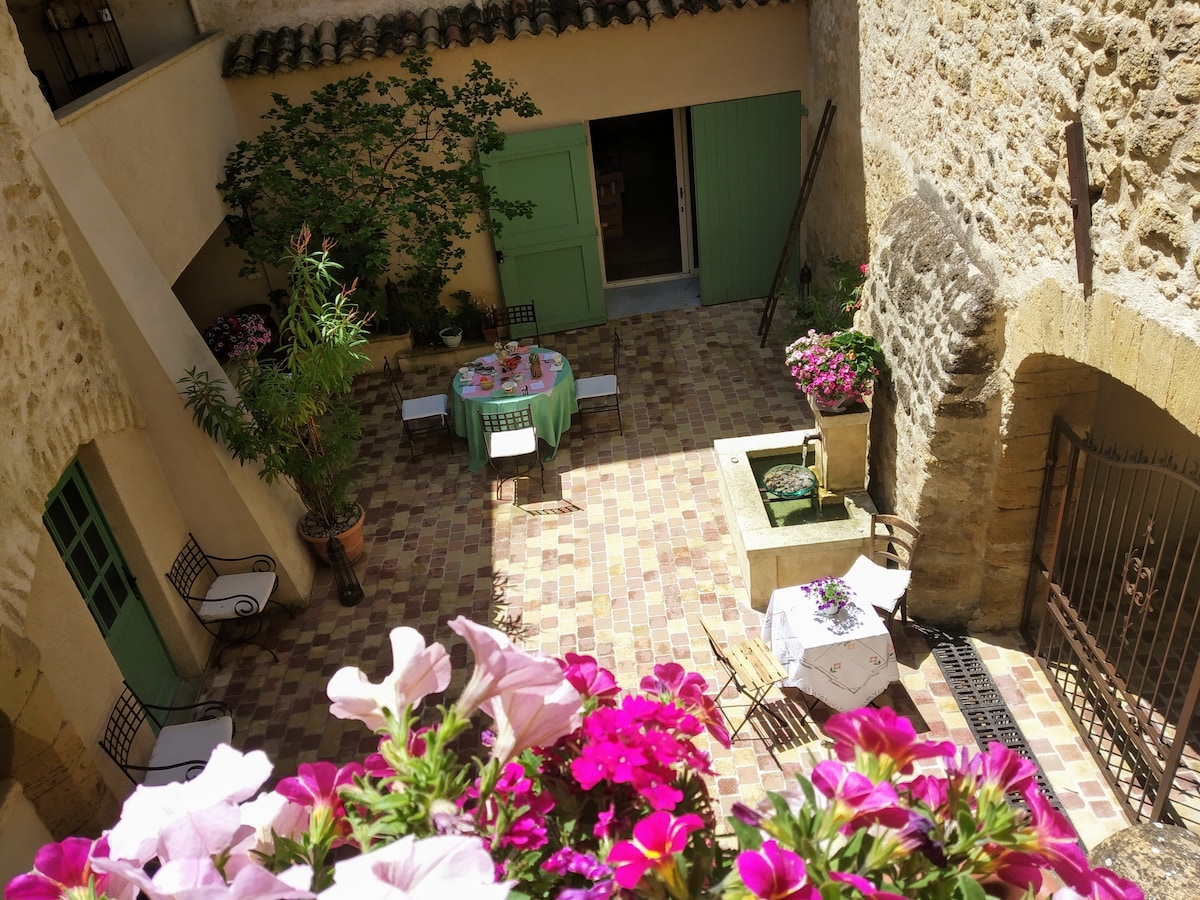 A charming courtyard is adorned with colorful flowers and elegant tables set for dining. Natural light fills the space, highlighting the textured stone walls and greenery. Various seating options are present, providing a cozy atmosphere for relaxation and gatherings.