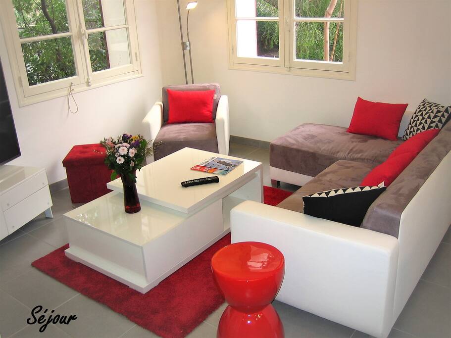Séjour climatisé avec petit canapé d'angle, fauteuil, table basse et TV.