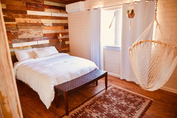 Bedroom off of the living room has a handmade recycled wood accent wall and more coziness with a hammock chair.
