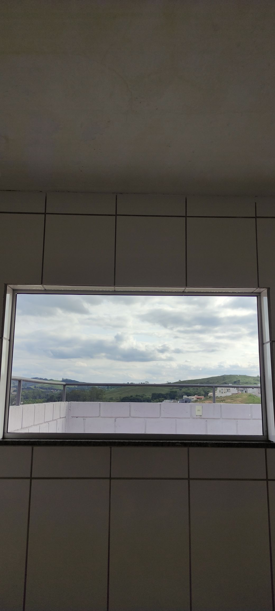 A window offers a view of rolling hills under a cloudy sky. The surrounding area includes a balcony with a low wall, providing a sense of openness to the outdoors.