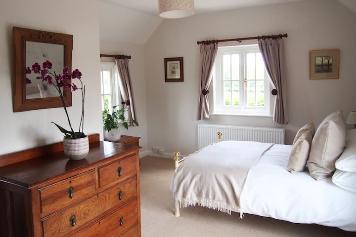 Dormitorio en planta alta con cama matrimonial y baño privado con ducha, con ventanas en tres lados. Espacio para colgar, secador de pelo y toallas y sábanas adicionales si es necesario. 