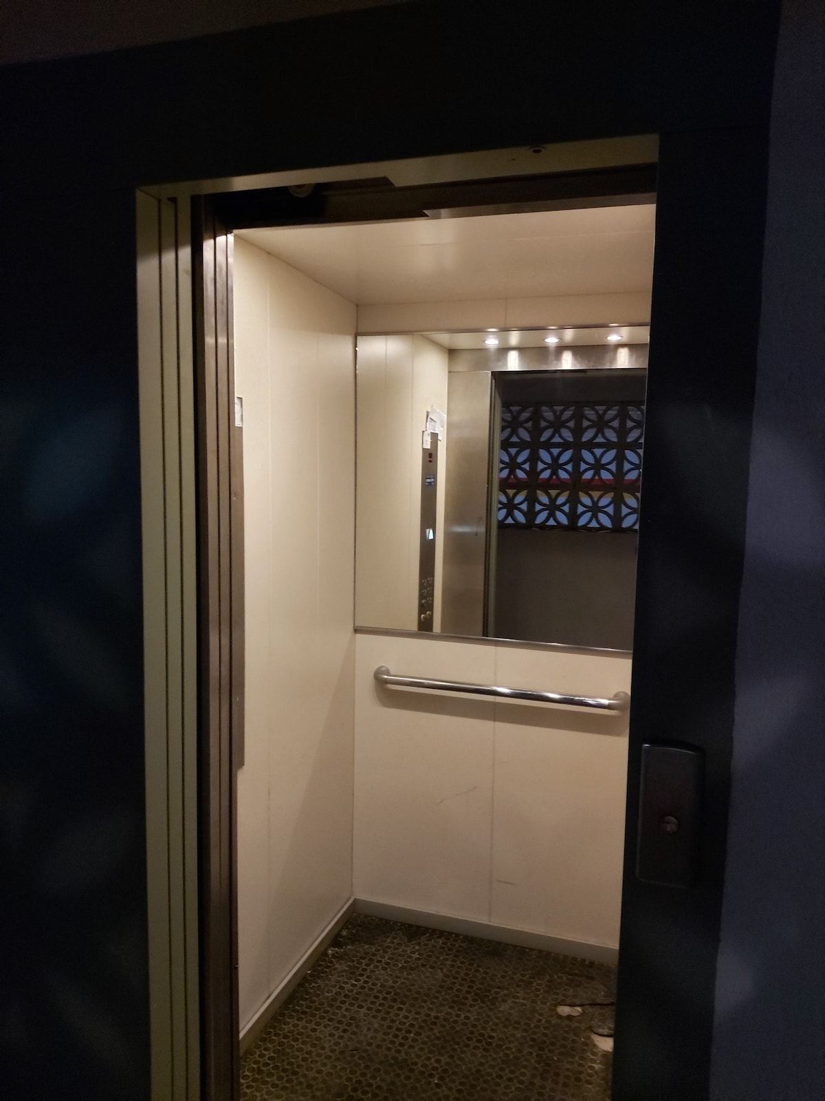An elevator is shown with a clean, white interior. Metal handrails are installed on one wall for assistance, and a patterned window allows soft light to filter in. The floor features a textured surface, enhancing overall safety and accessibility.