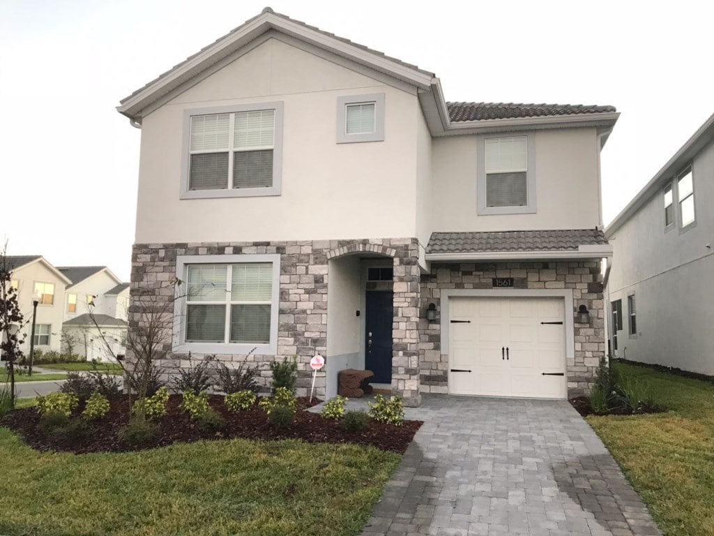 The two-story villa features a combination of light-colored stucco and stone accents on the exterior. Large windows allow for ample natural light, and a welcoming front porch is highlighted by tasteful landscaping, including neatly trimmed shrubs and colorful grass.