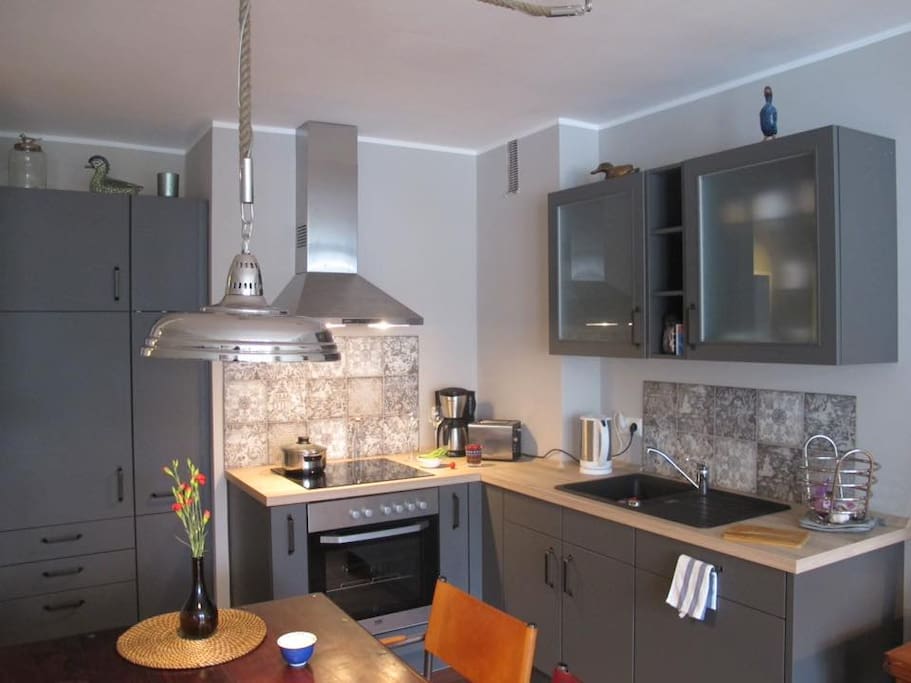 Eine moderne Einbauküche, offen zum Wohnraum, mit Backofen und 4-Platten-Ceranfeld, Geschirrspüler, Kühlschrank, Kaffemaschine und Geschirr