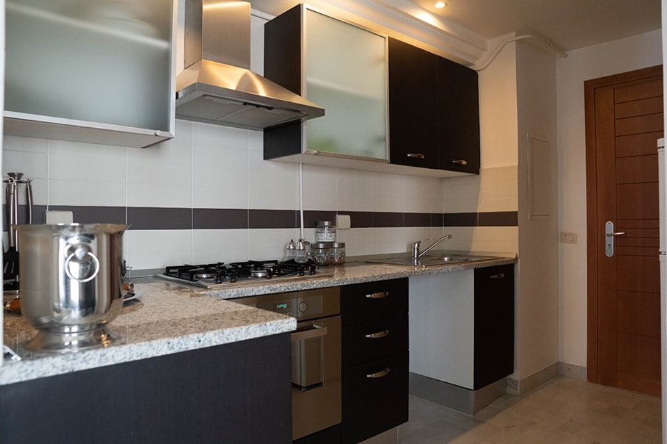 The kitchen features modern cabinetry with a minimalist design. A stainless steel stovetop and oven are present, along with a granite countertop. Essential appliances, including a saucepan and various utensils, are neatly arranged, providing a functional cooking space.