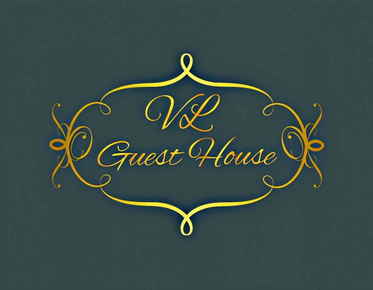 The image displays the logo of 'VL Guest House,' featuring elegant gold lettering against a dark green background. The design incorporates intricate decorative elements around the text, emphasizing the uniqueness of the guest house.