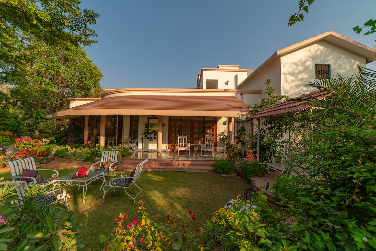 The exterior of the cottage showcases a charming garden filled with greenery and colorful flowers. A spacious terrace is adorned with comfortable seating arrangements, inviting guests to enjoy the serene atmosphere. The structure features a harmonious blend of traditional architecture and modern design elements.