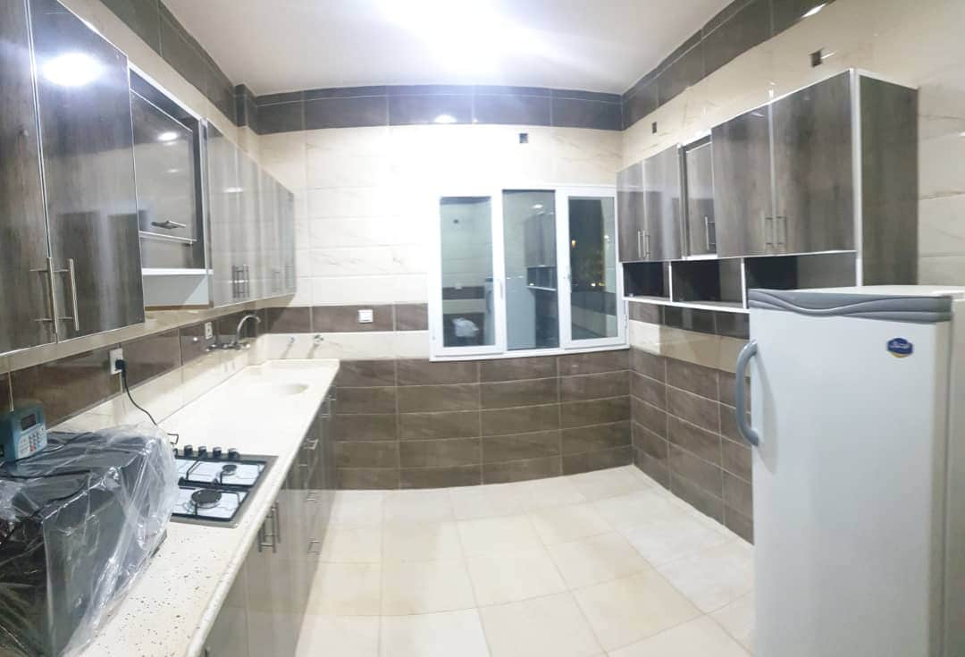 A well-appointed kitchen features sleek cabinetry with a mix of light and dark finishes. Countertops provide ample space for meal preparation, and appliances include a refrigerator and a gas stove. A window allows natural light to illuminate the area, enhancing visibility.