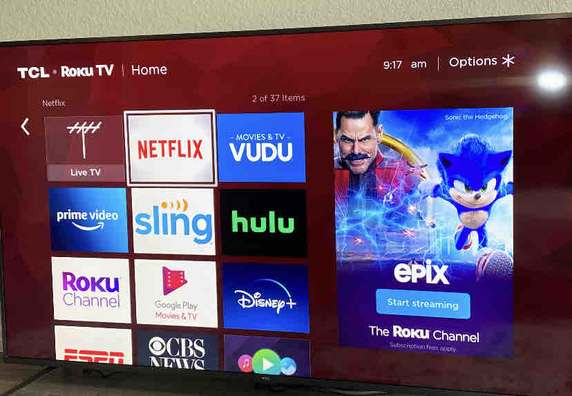 A smart television screen displays various streaming service options, including Netflix, Hulu, and Prime Video. The time is shown in the top right corner. The layout is organized in a grid format with bright colors highlighting each app.