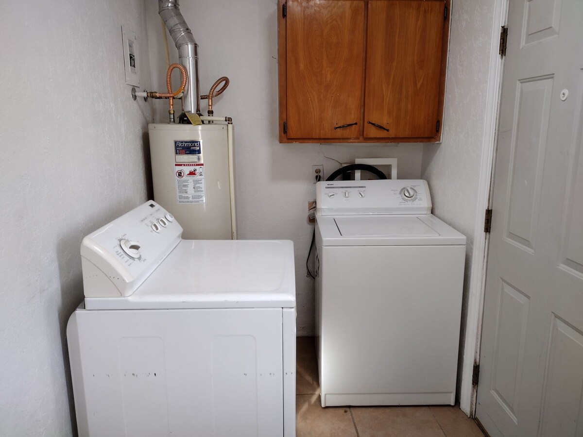 A practical laundry area is equipped with a washer and dryer, positioned side by side. Above the appliances, wooden cabinets provide additional storage. A water heater is visible to the left, adding to the functionality of the space.