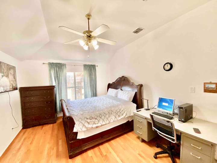 大きな窓、パソコンテーブル、椅子、キャビネット、テレビ、シーリングファンを備えた3つ目の寝室です。