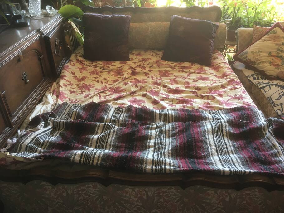 queen size bed from 1940s with tall air mattress next to sofa in same retro style with 52 inch flat panel Tv above wood cabinets