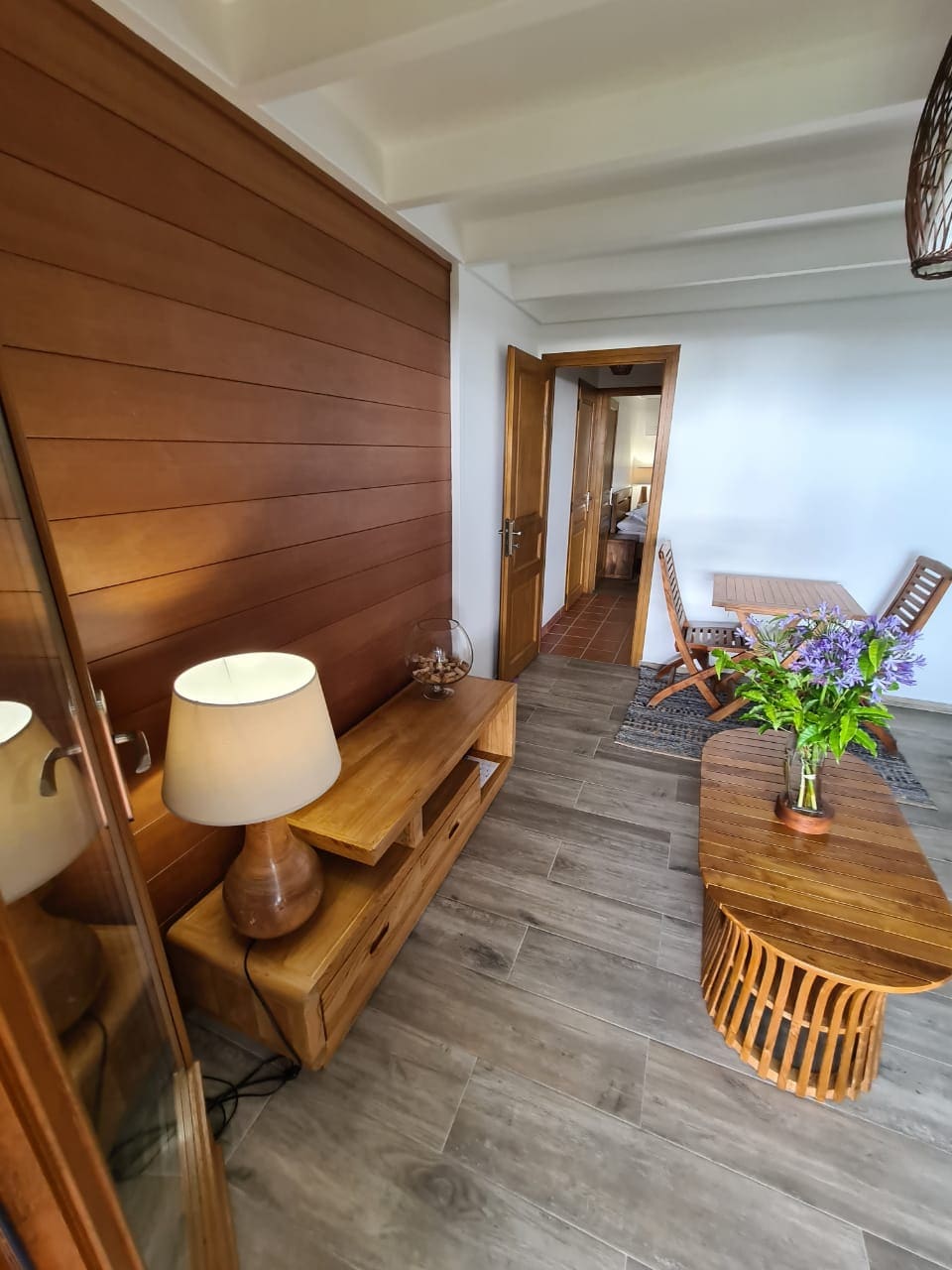 A welcoming entryway features wooden accents and a charming seating area. A lamp provides soft lighting next to a console table. A coffee table and two chairs invite relaxation, while a vase of fresh flowers adds a touch of color to the neutral decor.