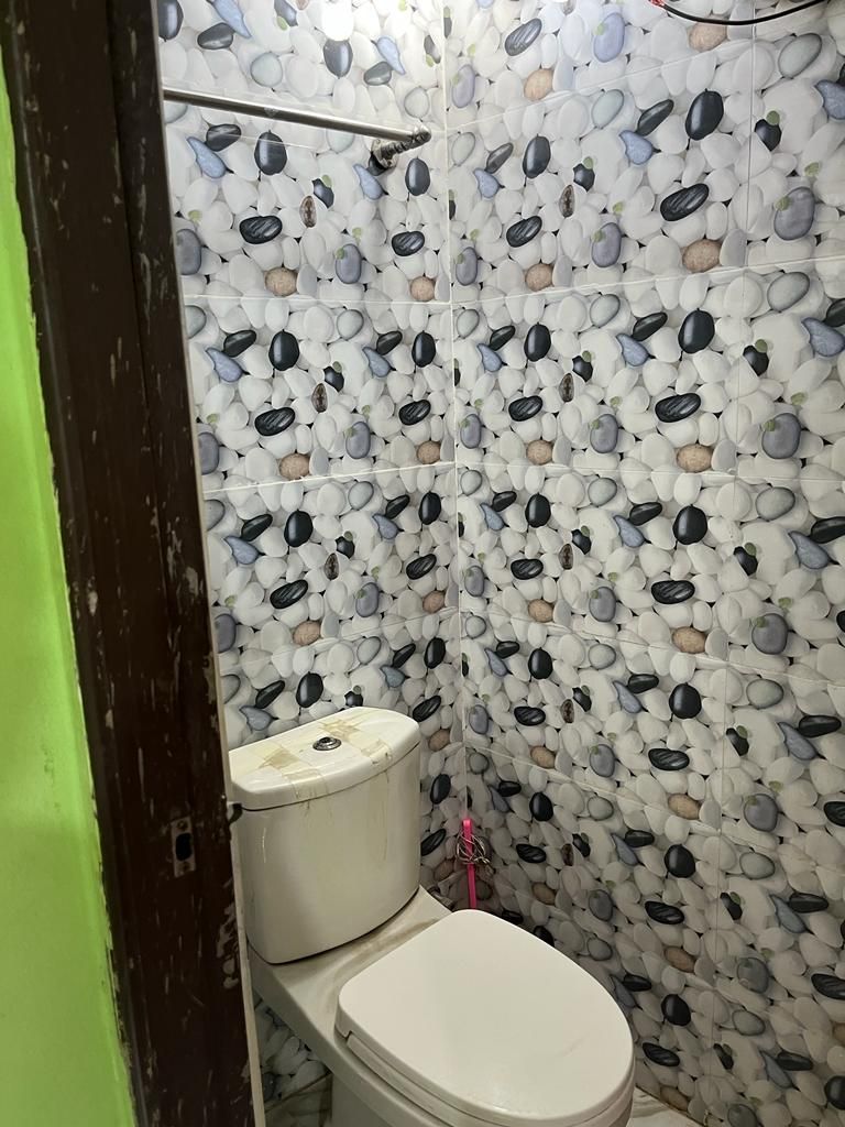 A compact half bathroom is shown, featuring a western toilet against a backdrop of patterned wallpaper. The space is designed for privacy, with a simple layout and natural light reflecting off the smooth surfaces.