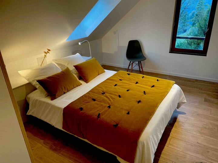Un grand lit  avec une literie  jaune confortable et douillette ,  deux grandes fenetres avec vue sur le jardin et les montagnes , une décoration moderne et chaleureuse.Les draps et le linge de lit sont fournis