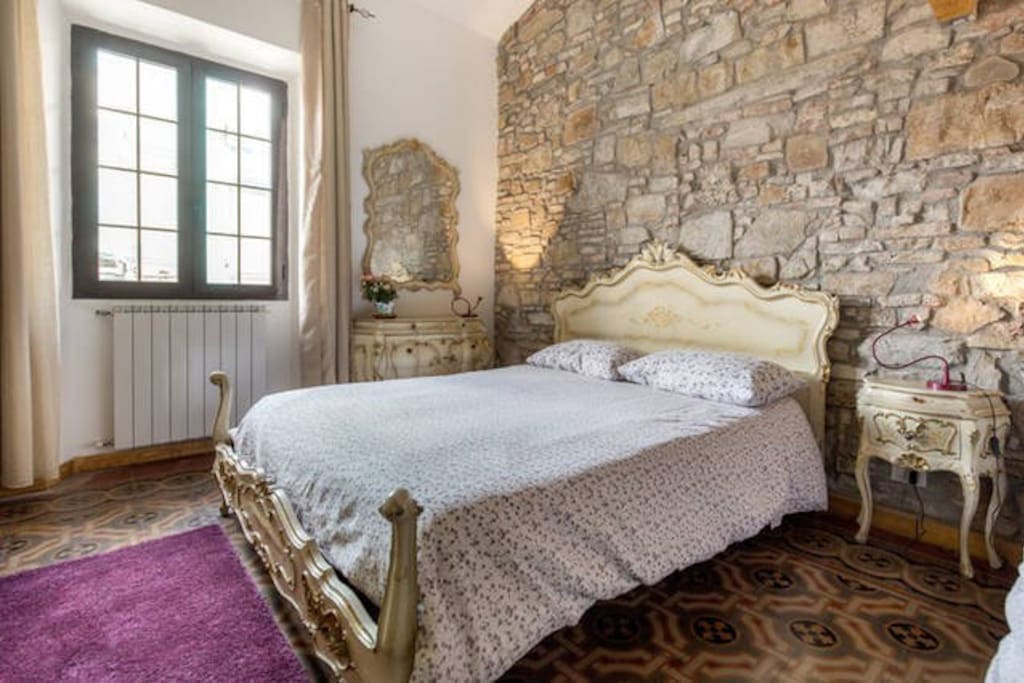 Ampia e luminosa camera, arredamento classico, con pareti in pietra e pavimento tradizionale.