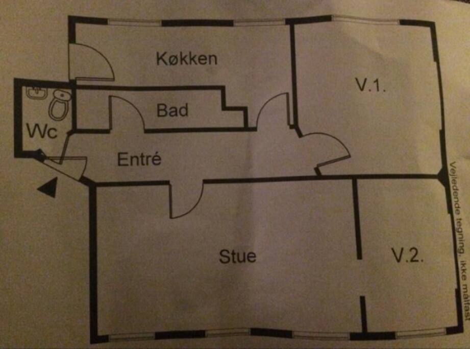 The plan view of the apartment. Køkken = kitchen, V.1 = the bed room 1, Bad = bathroom, Stue = living room, V.2 = the office