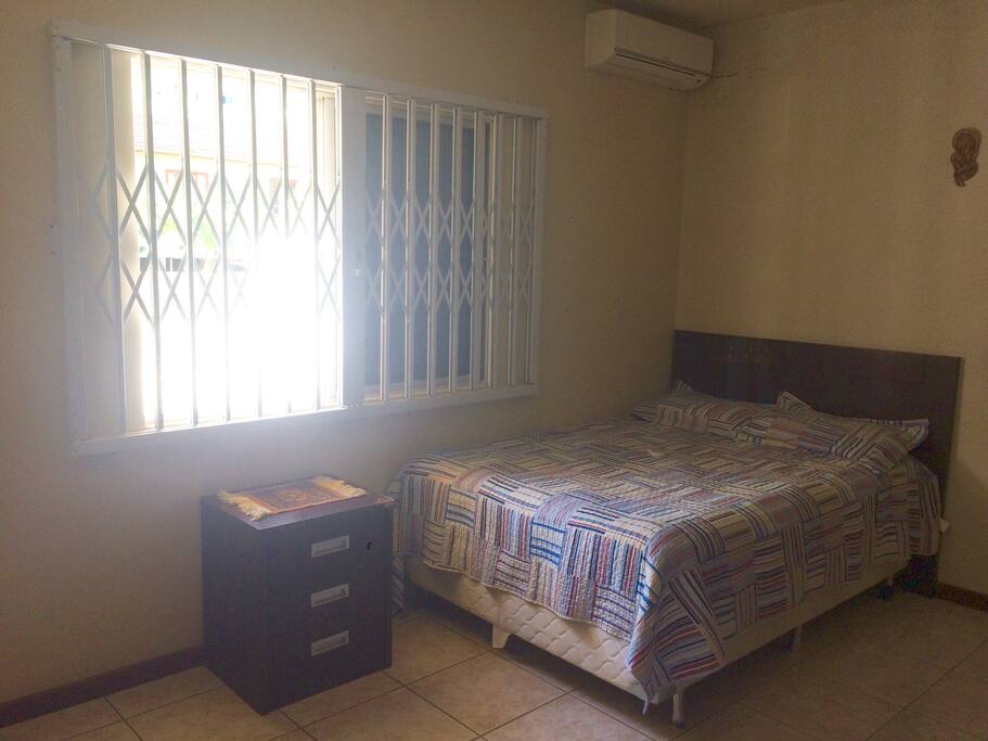 Suíte com cama de casal, ar condicionado, guarda roupa amplo, criados mudos com gavetas e balcão.