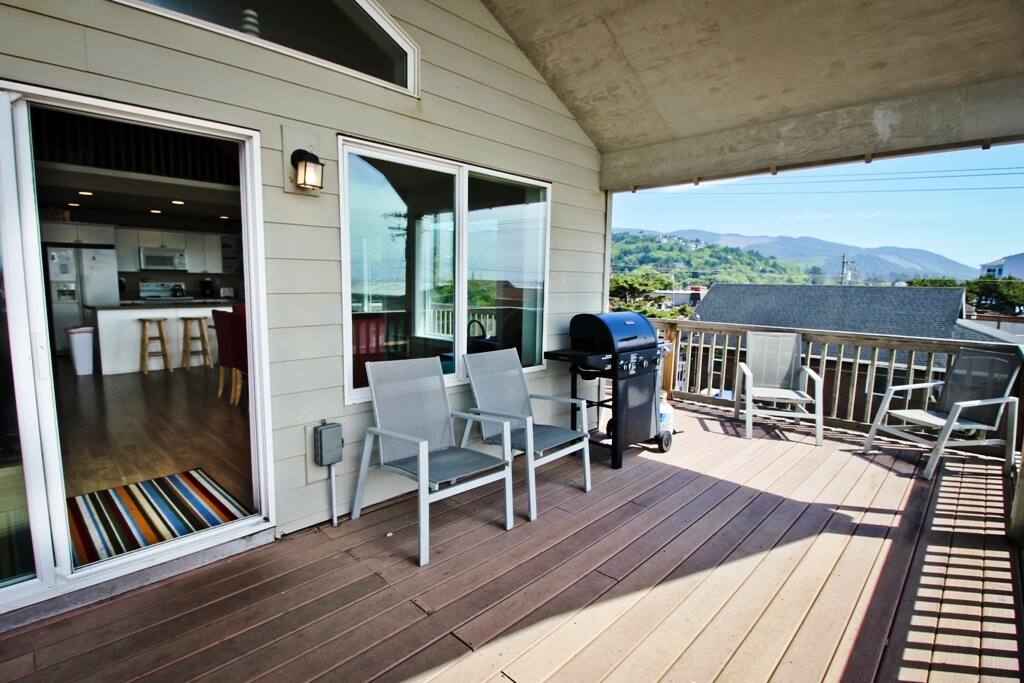Large upper level ocean facing wrap around deck with an ocean view hot tub, deck chairs, gas BBQ and two sliders into living area.