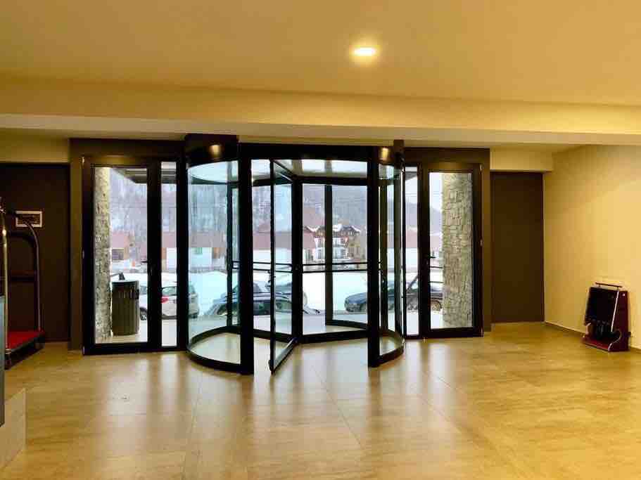 The entryway features a glass revolving door, allowing natural light to flood the space. A smooth, tiled floor extends throughout, while a glimpse of the snowy landscape is visible through large windows. The area is spacious and unobstructed, designed for easy access.