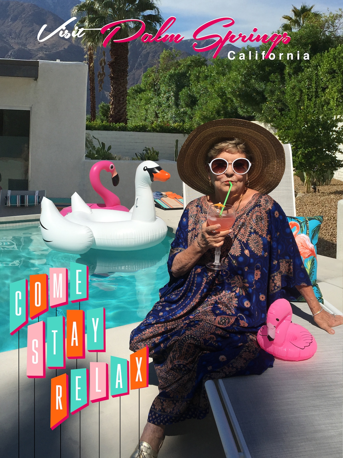 A guest is seated beside the pool, wearing a large sun hat and holding a drink. A vibrant kasbah-patterned cover-up adds a touch of style. Oversized inflatable swan and flamingo floaties rest in the pool, surrounded by the serene mountains in the background.