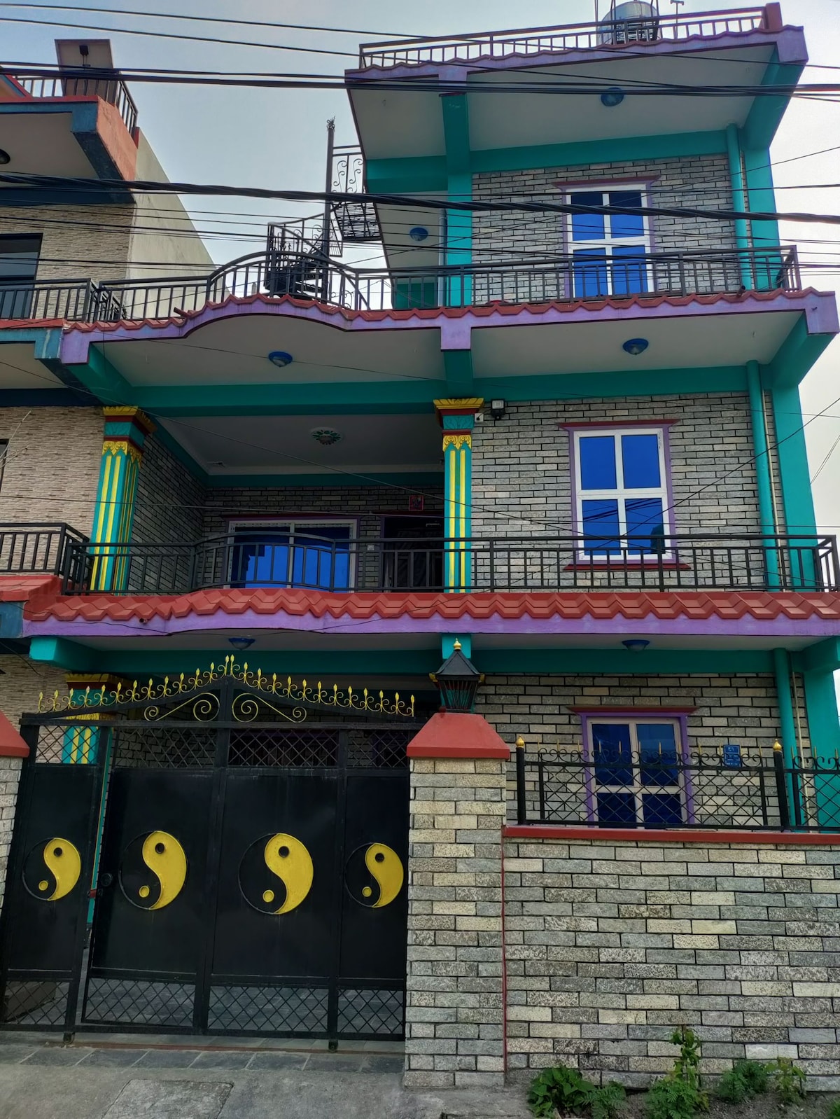 A multi-story building features a combination of brick and vibrant colored accents. The entrance is marked by a decorative black gate adorned with yin-yang symbols. Large windows on each level allow natural light to fill the interior spaces.