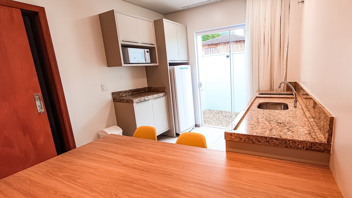 A modern kitchen area is featured, showcasing built-in cabinetry and a granite countertop. A dining table with two yellow chairs is positioned nearby. Natural light enters through a sliding door, which leads to a private outdoor space.