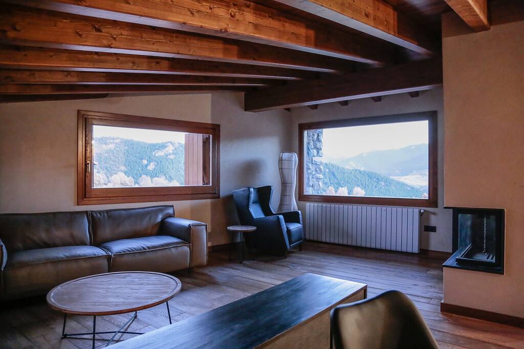 Comedor-salón amueblado con sofás y sillones de piel. Chimenea. Vistas al Cadí.