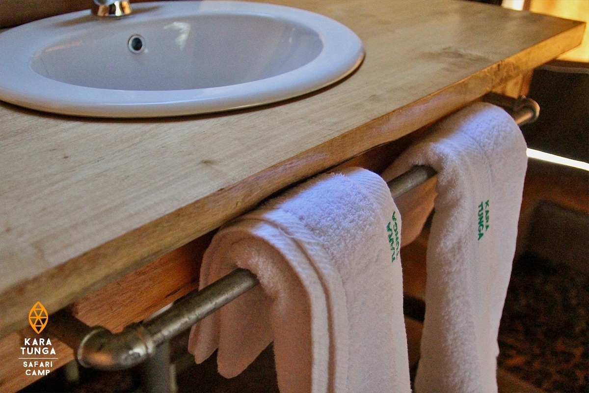 A clean and simple bathroom area is displayed, featuring a wooden countertop with a round sink. Two fresh white towels are neatly hung on a metal rod beneath the sink, contributing to the functional, rustic aesthetic.