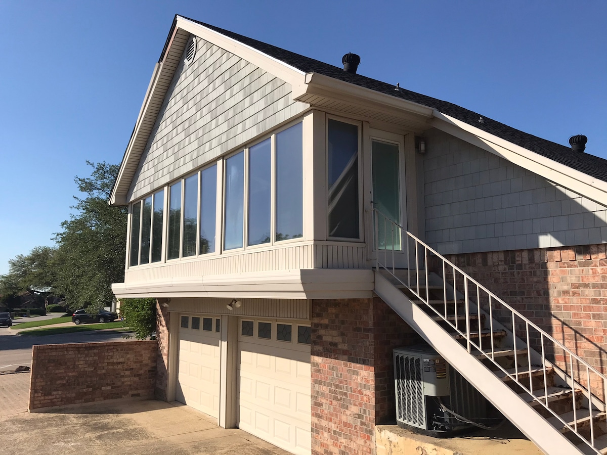 The exterior view presents a two-story building with a combination of brick and wood siding. A set of stairs leads to a covered entry, and large windows provide natural light to the upstairs space. A garage is visible beneath the structure.