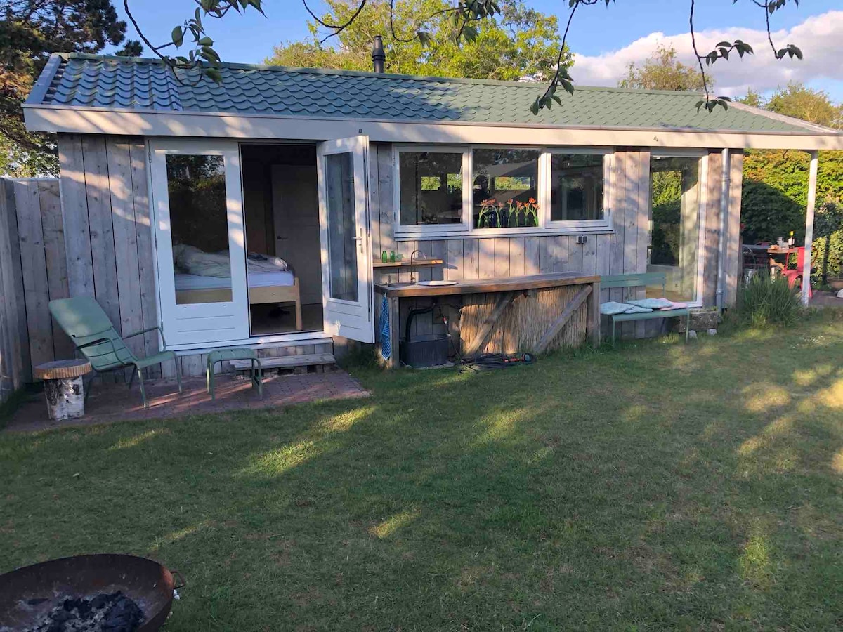 A charming holiday home is surrounded by a spacious garden. Large windows frame the entryway, allowing natural light to fill the interior. Outdoor seating areas are available for relaxation, with a barbecue and a grassy area ideal for recreation.