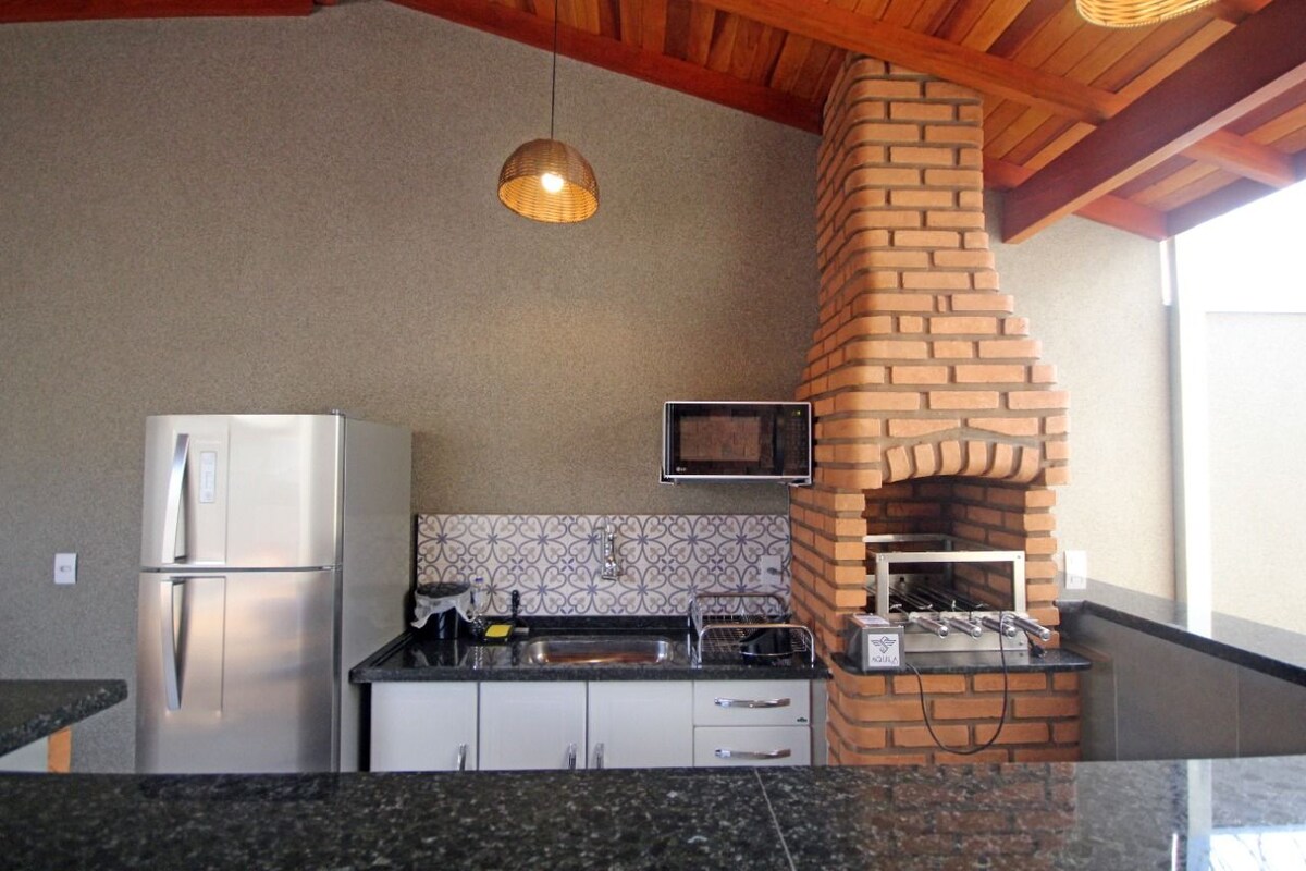 An open kitchen area features modern appliances including a refrigerator and microwave. A brick fireplace adds character, while a sleek countertop complements the space. Decorative tiles line the backsplash, providing a subtle contrast to the overall design.