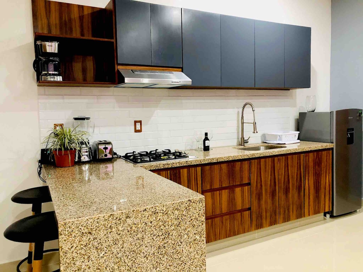 A modern kitchen features sleek cabinetry in dark tones, complemented by wooden accents. A gas stove and stainless steel sink are highlighted, with a refrigerator visible on one side. A countertop with seating for two is present, enhancing the functionality of the space.