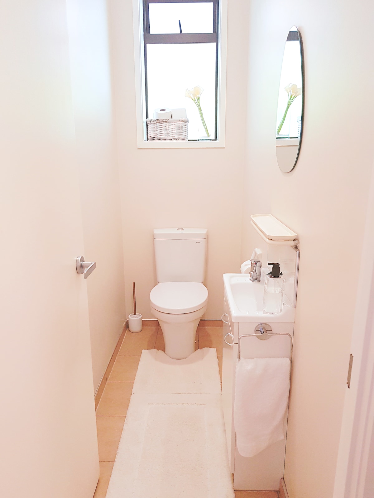 A compact bathroom space is visible, featuring a white toilet and a small sink with a mirror above. Soft towels are neatly arranged, and an elegant basket adds a touch of decor. Natural light filters through a window, enhancing the serene environment.