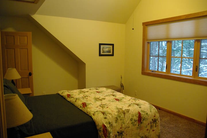 Главната спална соба на горниот кат со брачен кревет и прекрасни шуми и поглед кон реката.
