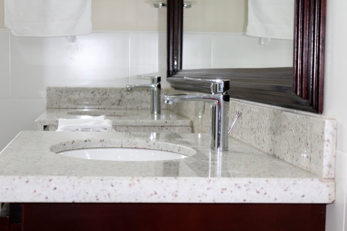 The bathroom vanity features a polished granite countertop with dual sinks and modern faucets. Two wall-mounted mirrors reflect the clean design, while soft towels are neatly placed beside the sinks. The overall aesthetic is bright and functional, enhancing the bathroom's serene ambiance.