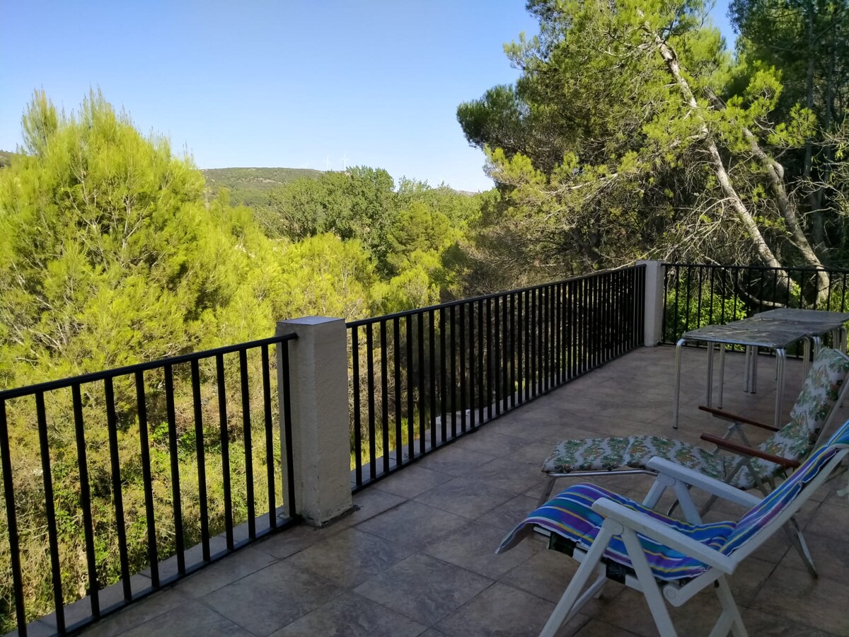 A spacious balcony offers views of lush greenery and distant hills, with sturdy railings ensuring safety. Two lounge chairs are positioned for relaxation, and a table is available for outdoor dining. The serene setting enhances the connection with nature.