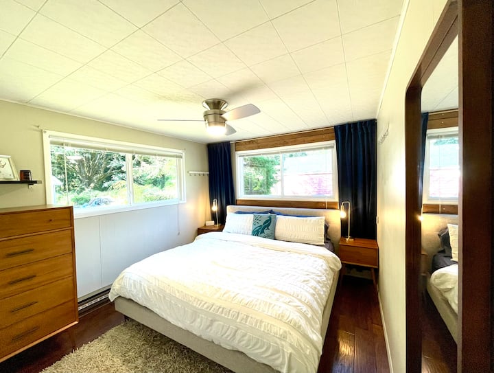 The king bedroom has a World-Class Beautyrest mattress on an upholstered bed against a wood accent. Mid-century West Elm nightstands and dresser give you plenty of storage. Stay cool with the 3-speed ceiling fan. Closet to the left.