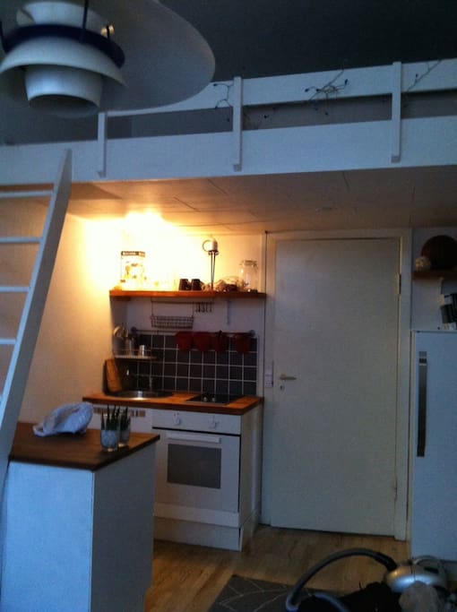 room with a small kitchen and stairs to the loft