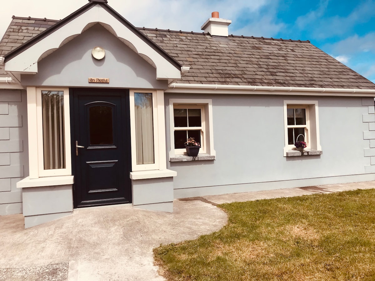 The exterior of the bungalow features a welcoming entrance with a dark front door framed by light grey walls. Flower pots adorn the window sills, and the roof has a charming overhang. A well-maintained lawn provides additional greenery in front.