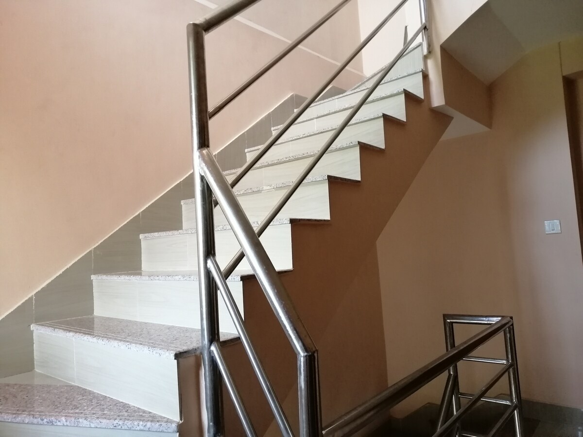 A light-colored staircase is captured, featuring polished steps with a subtle granite texture. Chrome railings provide support along the gently ascending path, leading to an upper level. The walls are painted in a soft shade, contributing to a welcoming ambiance.