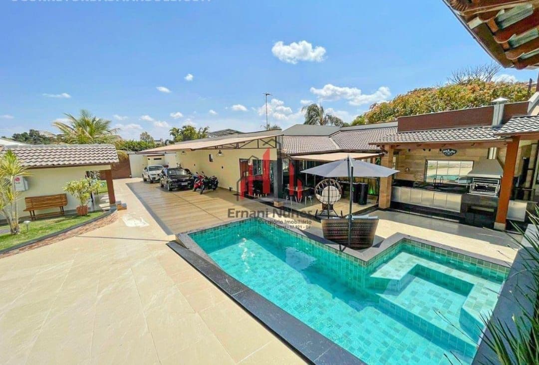 An outdoor area features a heated pool with turquoise tiles, surrounded by a spacious deck. A shaded seating area with a large umbrella and a well-equipped barbecue area are visible, alongside a landscaped lawn. Several vehicles are parked nearby.