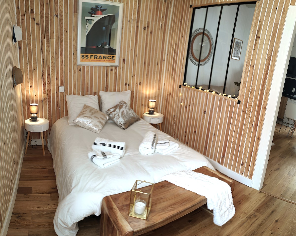 A cozy bedroom features wooden paneling and warm lighting. A spacious bed is adorned with decorative pillows and placed against the wall. Small nightstands flank the bed, each holding a lamp. A wooden bench at the foot of the bed adds a practical touch.