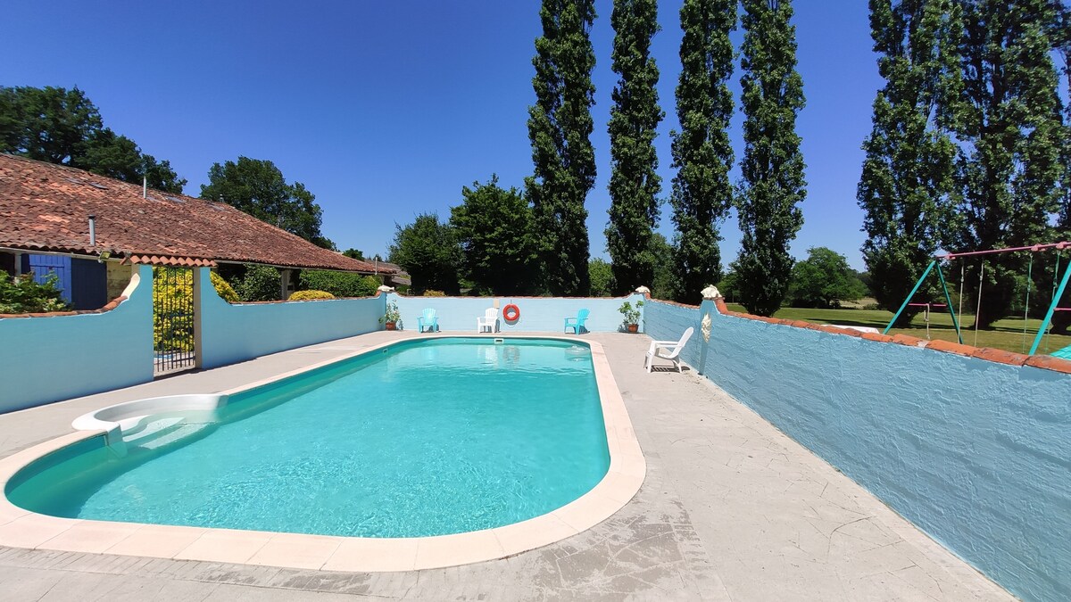 A clear blue pool is surrounded by a spacious patio. Colorful chairs are positioned nearby, while a swing set adds to the outdoor area. Lush green trees frame the scene, creating a serene and inviting atmosphere for relaxation.