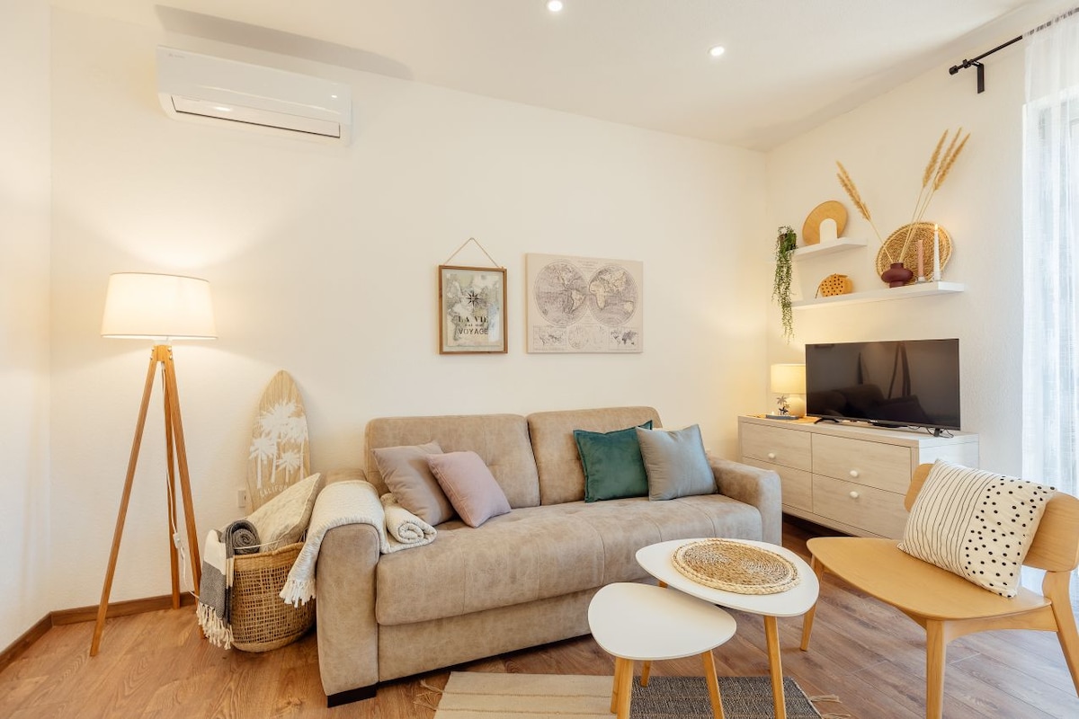 A cozy living space is shown, featuring a comfortable sofa adorned with decorative pillows. A wooden coffee table and a light chair are nearby, enhancing the inviting atmosphere. Soft lighting from a standing lamp illuminates the room, while wall decor adds a touch of charm.