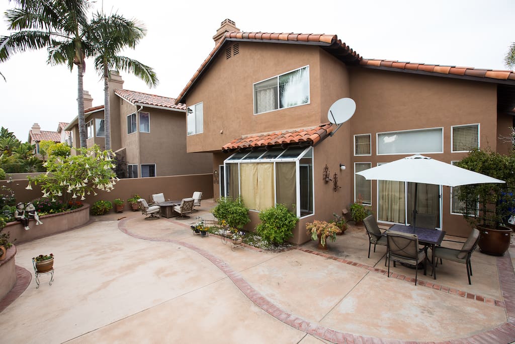 Backyard view of home, including outdoor table set with umbrella, BBQ, and lounging chairs.